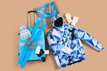 Suitcase with winter accessories and snowflakes on beige background, top view