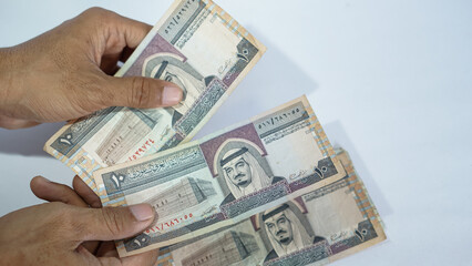 hands count saudi riyal banknotes at a white background reflecting finance, cash and currency exchange