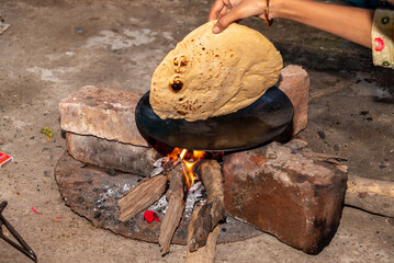 A village woman makes bread on the stove. cooking bread in clay stove , chula , makeing bread , roti , in village