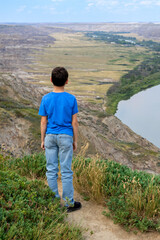 Fototapeta premium Boy is stanfing on the top of the hill and looking at the river. Red deer river, Drumheller, Alberta, Canada.
