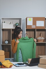 vlogger, blogger small SME business asian beautiful woman using mobile phone video call for sell clothes live stream selling online, show product present detail at home office, entrepreneur ecommerce