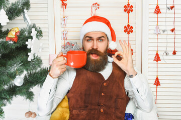 Merry Christmas. Santa Claus retro man drinking coffee. Happy New Year. Xmas holiday celebration. Santa man in retro style with mug. Showing ok. Delicious hot wine for Christmas. Man celebrate Xmas