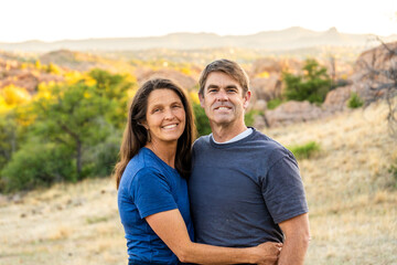 Smiling couple enjoying a serene sunset in a picturesque outdoor setting with mountains in the...