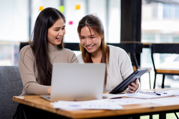 Two asian confident business people point to graphs and charts to analyze market data, balance sheet, account, net profit to plan new sales strategies to increase production capacity.	
