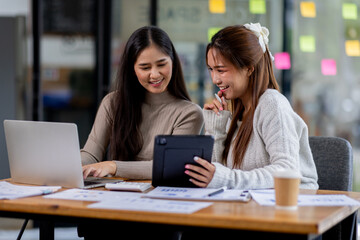 Two asian confident business people point to graphs and charts to analyze market data, balance sheet, account, net profit to plan new sales strategies to increase production capacity.	
