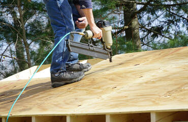 handyman using nail gun to install shingle to repair roof
