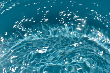 Blue water with ripples on the surface. Defocus blurred transparent blue colored clear calm water surface texture with splashes and bubbles. Water waves with shining pattern texture background.