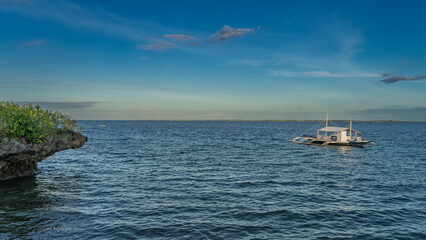 The traditional double-outrigger dugout Filipino bangka boat is anchored in the ocean. Ripples on...