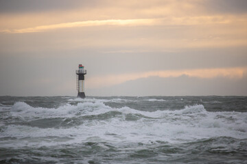 a lighthouse stands in the storm. Wild sea in a long exposure. Sunset on a coast with many rocks in...