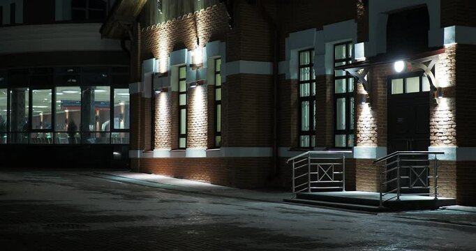 Night city.  Beautifully illuminated by hanging lanterns, the brick wall of the old city station building next to the modern annex. Siberia. Hand held, panning.