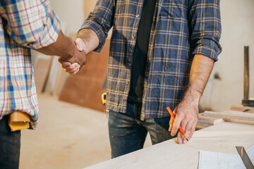 Close-up of two construction carpenters shaking hands in a woodshop. Ideal for teamwork, cooperation, and beginning of work at a factory or workshop setting, National Carpenters Day