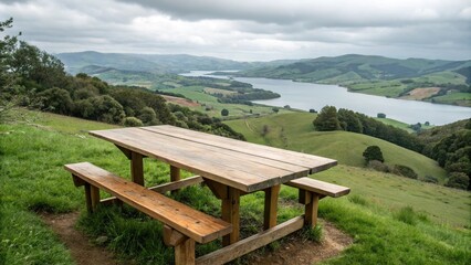 A large wooden table placed on a hillside overlooking a tranquil green valley with rolling hills and a distant lake, scenic landscape, outdoor decor, hillside view, wooden furniture