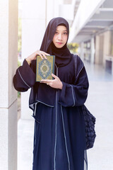 A beautiful Muslim student wearing abaya niqab traditional clothes portrait standing and hold Quran...