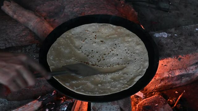 A village woman makes bread on the stove. cooking bread in clay stove , chula , makeing bread , roti , in village