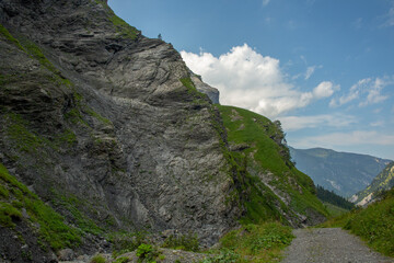 Empty road in alpine valley, rough and steep rocks of mountain slope, Switzerland
