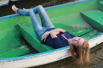 Young cute barefoot girl model in a blue jeans traveling on the boat station at sunset.
