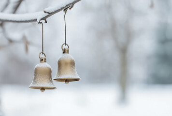 Obraz premium Zwei schneebedeckte goldene Glocken, hängend an Ast in winterlicher Landschaft, Symbol für festliche Weihnachten, Dekoration und Karte