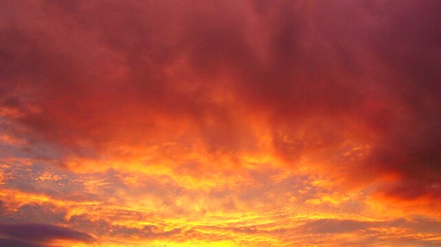 Yellow orange red sunset sky clouds. Soft warm hue of yellow and red casts serene and beautiful atmosphere. Gentle rays of setting sun paint horizon. Dramatic sunset. Real time, cumulus clouds