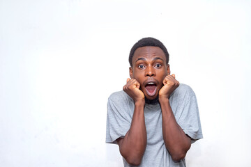 A young man in a grey t-shirt shows a surprised expression with hands on cheeks. His shocked face conveys astonishment and surprise against a plain white background, highlighting his emotions.