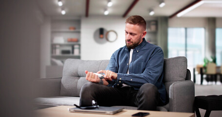 Young Man Sitting On Sofa Checking His Blood Pressure