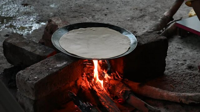 A village woman makes bread on the stove. cooking bread in clay stove , chula , makeing bread , roti , in village