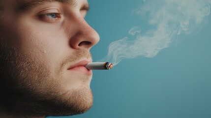 A young man exhales smoke while holding a cigarette, with a soft focus on his contemplative expression against a blue background.