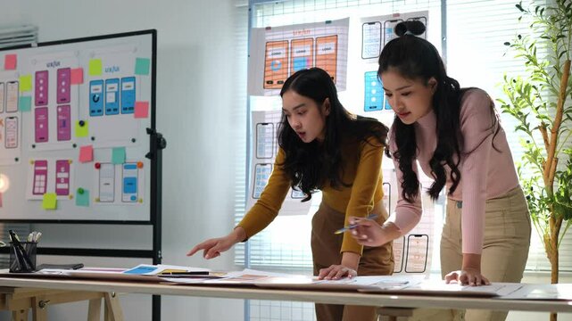 Teamwork, Two female designers working with UX developer and UI designer at desk in modern office. Creativity working on mobile responsive website. Developing wireframe design on smartphone screen.