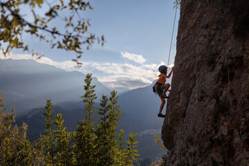 Fototapeta premium rock climber boy. child trains rock climbing at summer camp. children's summer camp. sport in nature.