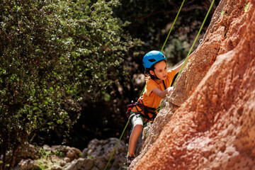 sport in summer camp. a child is rock climbing at a summer camp. rock climber boy. sport in nature on a sunny day. cute teenager climbs a rock with a belay. active holidays.