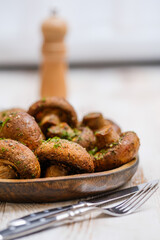 Freshly cooked mushrooms served on a wooden plate with a pepper grinder in the background