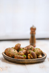Deliciously roasted mushrooms served on a wooden plate with herbs and pepper on a rustic table