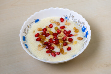 Delicious homemade payesh or payasam, served in a white bowl on a wooden background. Cooked with milk, sugar or jaggery, and rice, it's garnished with cashew nuts, raisins, pomegranate, and peanuts.