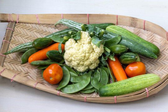 A traditional bamboo cane-woven Kula or Kulo filled with fresh vegetables, including cauliflower, carrots, cucumber, snake gourd, green chilies, beans, tomatoes, and pointed gourd.
