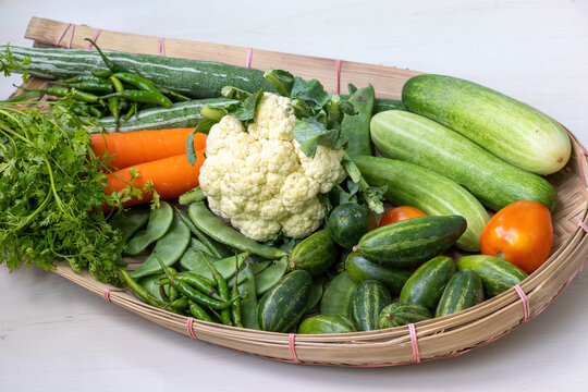 A traditional bamboo cane-woven Kula or Kulo filled with fresh vegetables, including cauliflower, carrots, cucumber, snake gourd, coriander leaves, green chilies, beans, tomatoes, and pointed gourd.