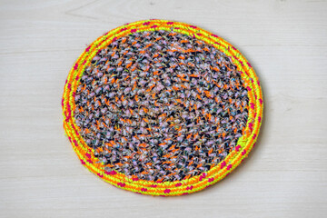 Handmade colorful round table runner on wooden background. Handcrafted woven fabric mat for home...
