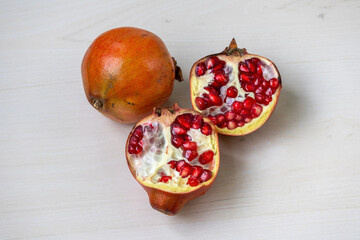 A whole pomegranate and a half on a light wooden surface.