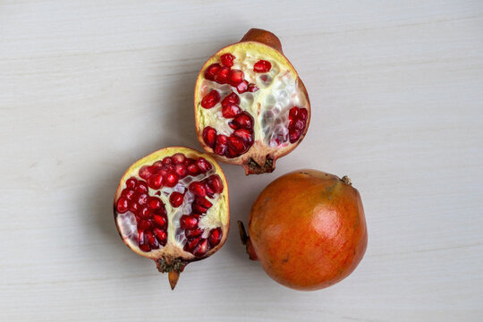 A whole pomegranate and a half on a light wooden surface. Top view.