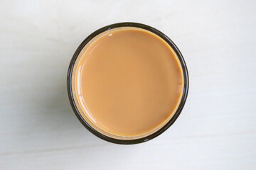 Hot milk tea or dudh cha in a glass cup, kept on a light wooden surface. Top view.