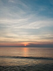 Obraz premium a breathtaking sunset at the horizon of the sea. The sky is painted with hues of orange, pink, and purple as the sun slowly descends, casting a warm glow over the tranquil waters.