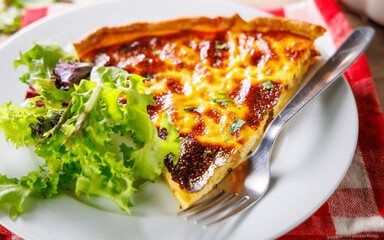 close up on savoury slice of quiche lorraine with lettuce on plate
