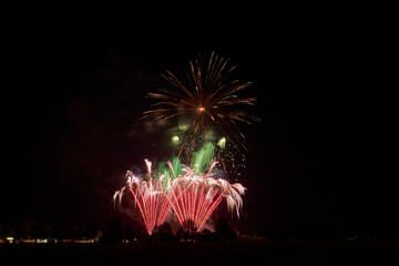 Fireworks explode in the night sky, illuminating the darkness with bright green and red sparks over...