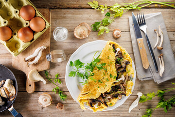 fluffy omelet with mushrooms on plate with ingredients on wooden background