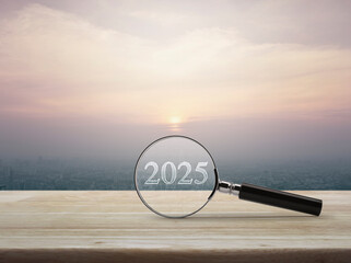 Magnifying glass with 2025 text and financial graph on wooden table over modern city tower and skyscraper at sunset, vintage style, Business happy new year 2025 research concept