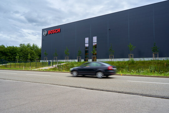 Moving car on a road in front of a large Bosch building, surrounded by trees under a cloudy sky, symbolizing urban development. Wernau, Germany, Europe.