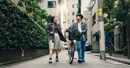 Obraz premium Fashion, walking and bike with Japanese couple in city for streetwear, genz style and travel. Date, urban and love with asian man and woman talking in outdoors for bonding, casual and cool together