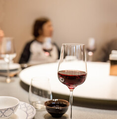 A glass of red wine on the restaurant table, an out-of-focus woman on the other side of the table.