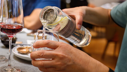 Hands of a man pouring water into a glass. Red wine glass on the side. Drinking water at the restaurant.