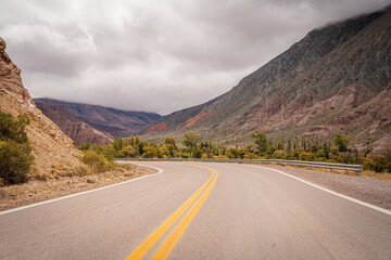 Scenic road winds through a mountainous landscape under a cloudy sky.