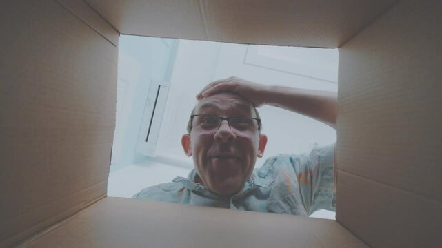 Man with hand on head reacts in amazement as he inspects the contents of a box from a low perspective in 4K slow motion 120fps