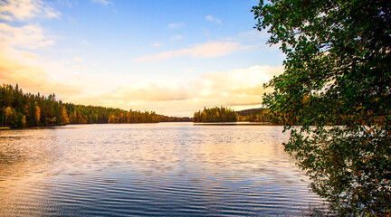 Sunrise at lake Gränsjön in Swedish municipality Arvika in Värmland important part of Göta river main catchment area. With border of forests in autumn colors and warm colored cloud sky